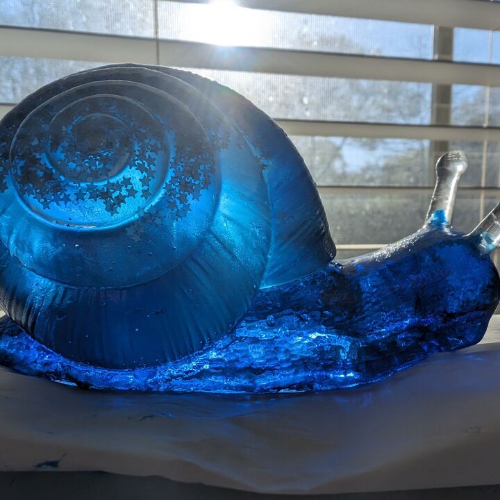 Translucent blue resin snail with a swirled shell, lit by a window